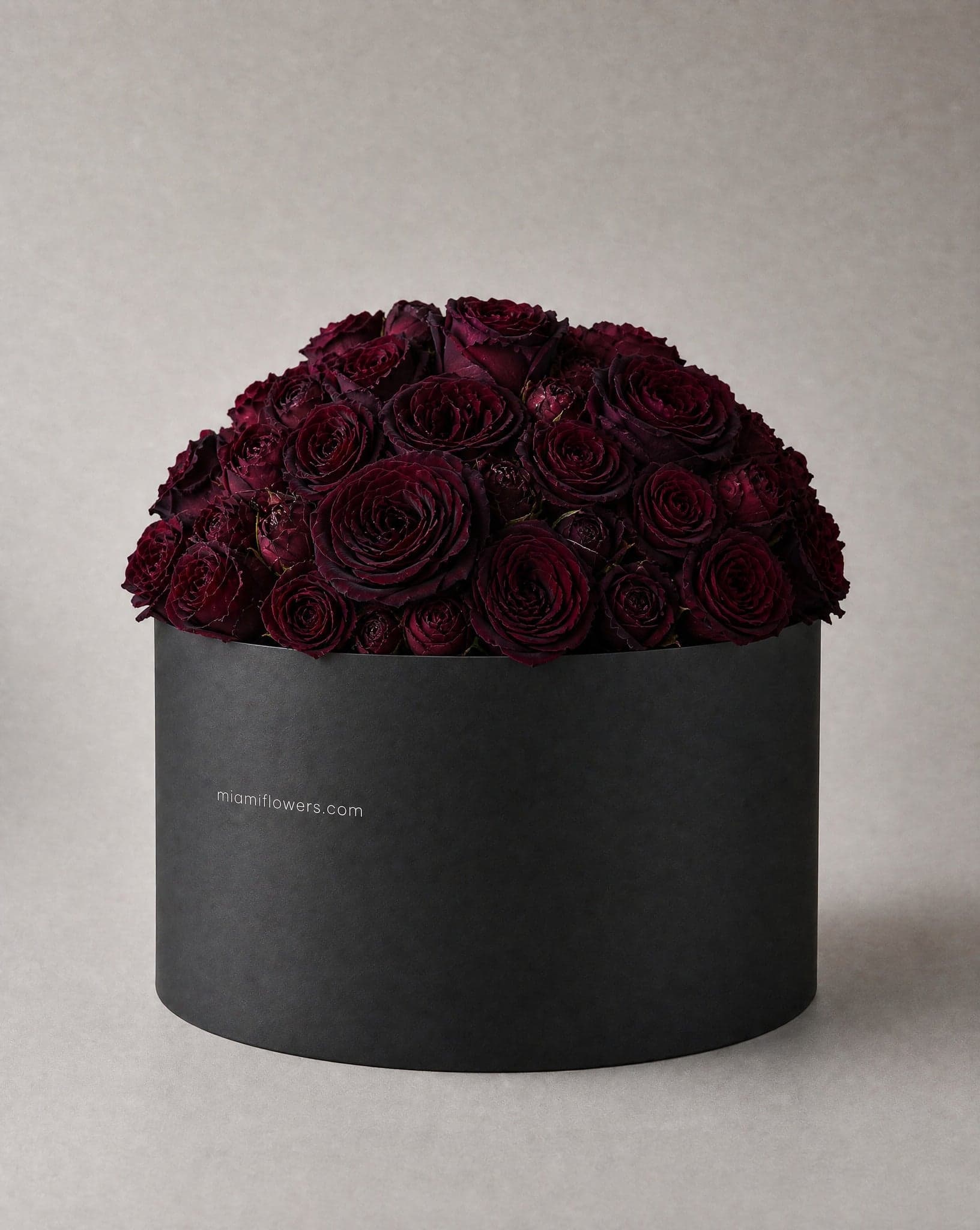 Burgundy and near black roses in a tall matte black oval box printed with miamiflowers.com