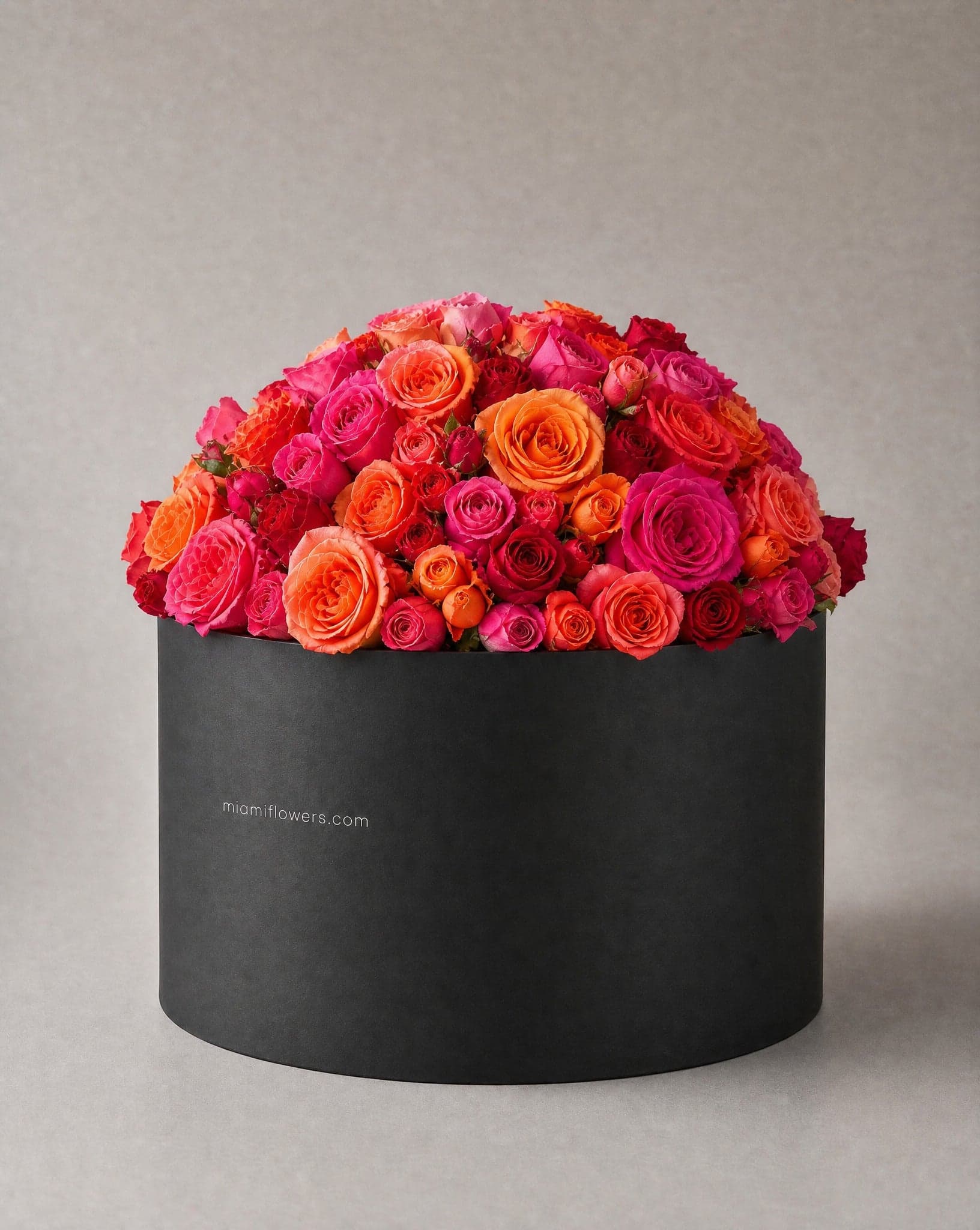 Bright pink, coral and orange roses in a tall matte black oval box printed with miamiflowers.com