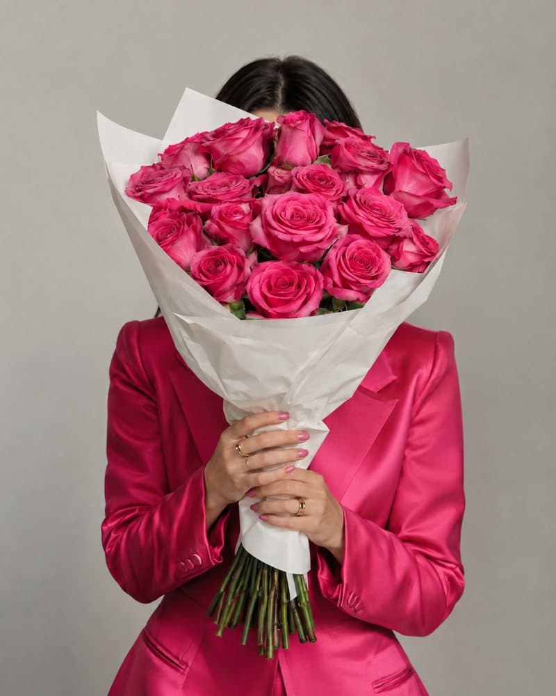 Woman in a pink blazer holding hot pink roses in front of her face