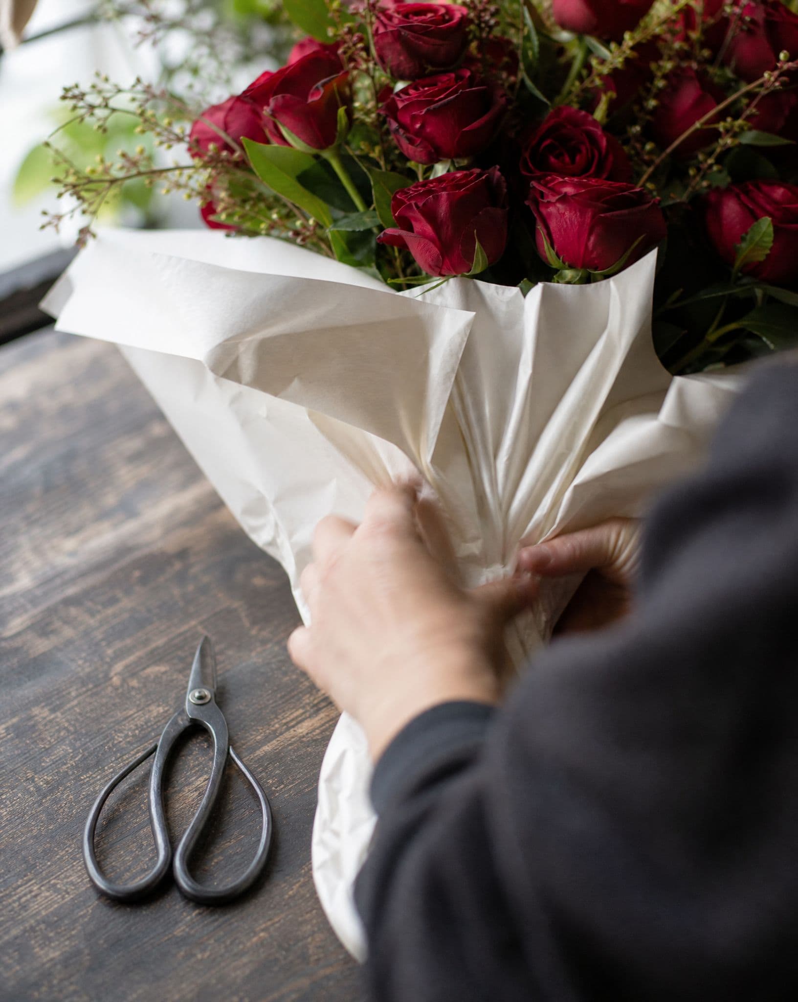 A florist wrapping red roses in white paper