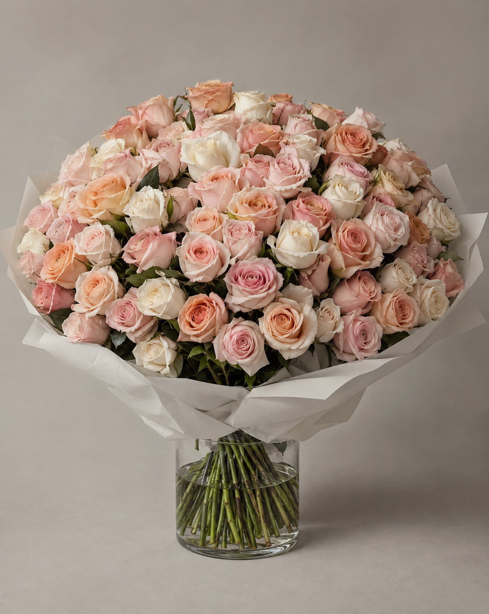 Pastel roses wrapped in white tissue in a clear glass vase