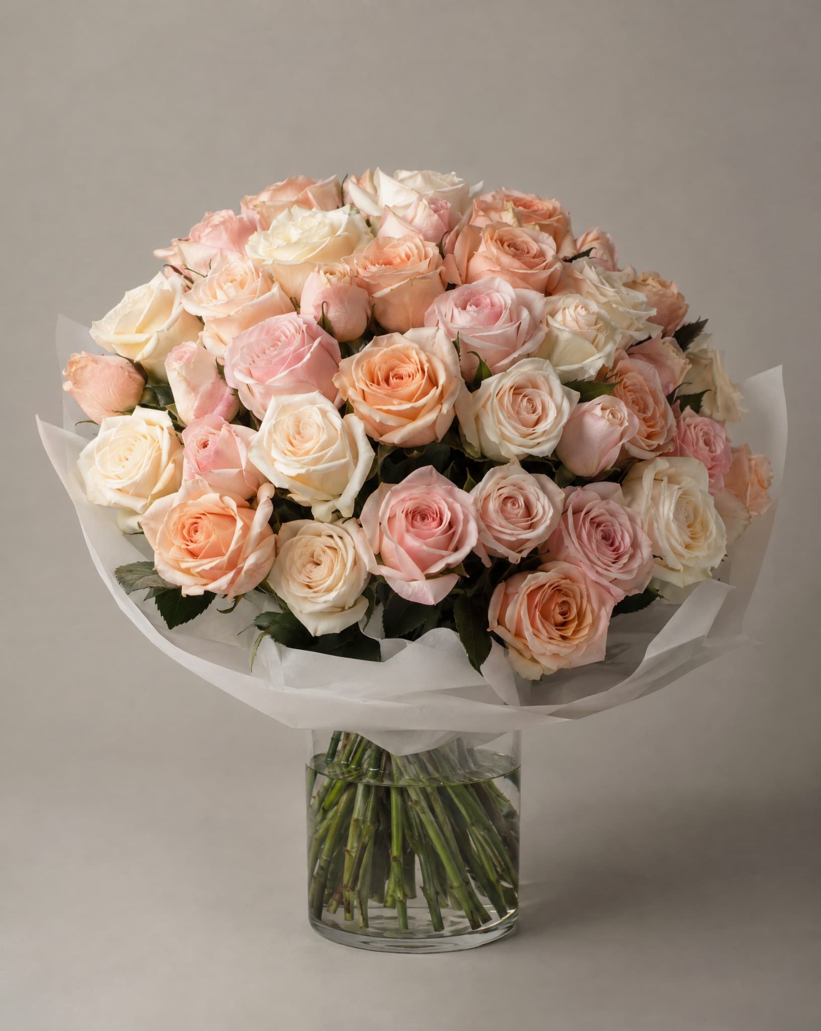 Pastel roses wrapped in white tissue in a clear glass vase