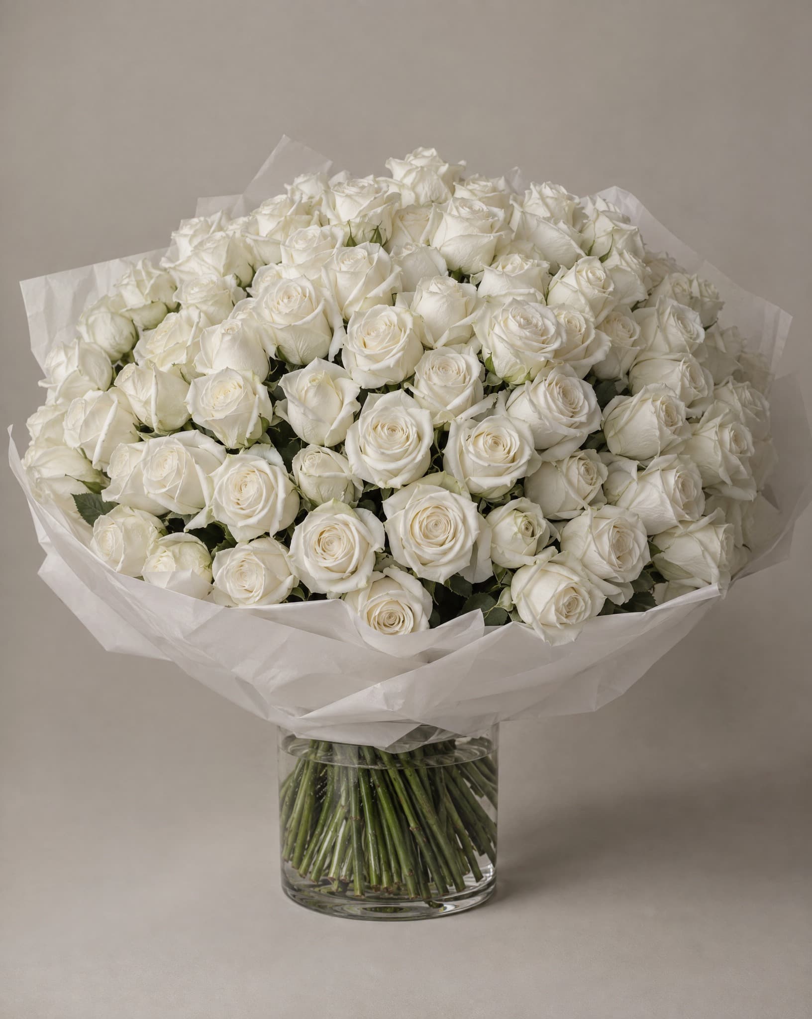 Rosas blancas envueltas en papel de seda blanco, en un florero de vidrio transparente