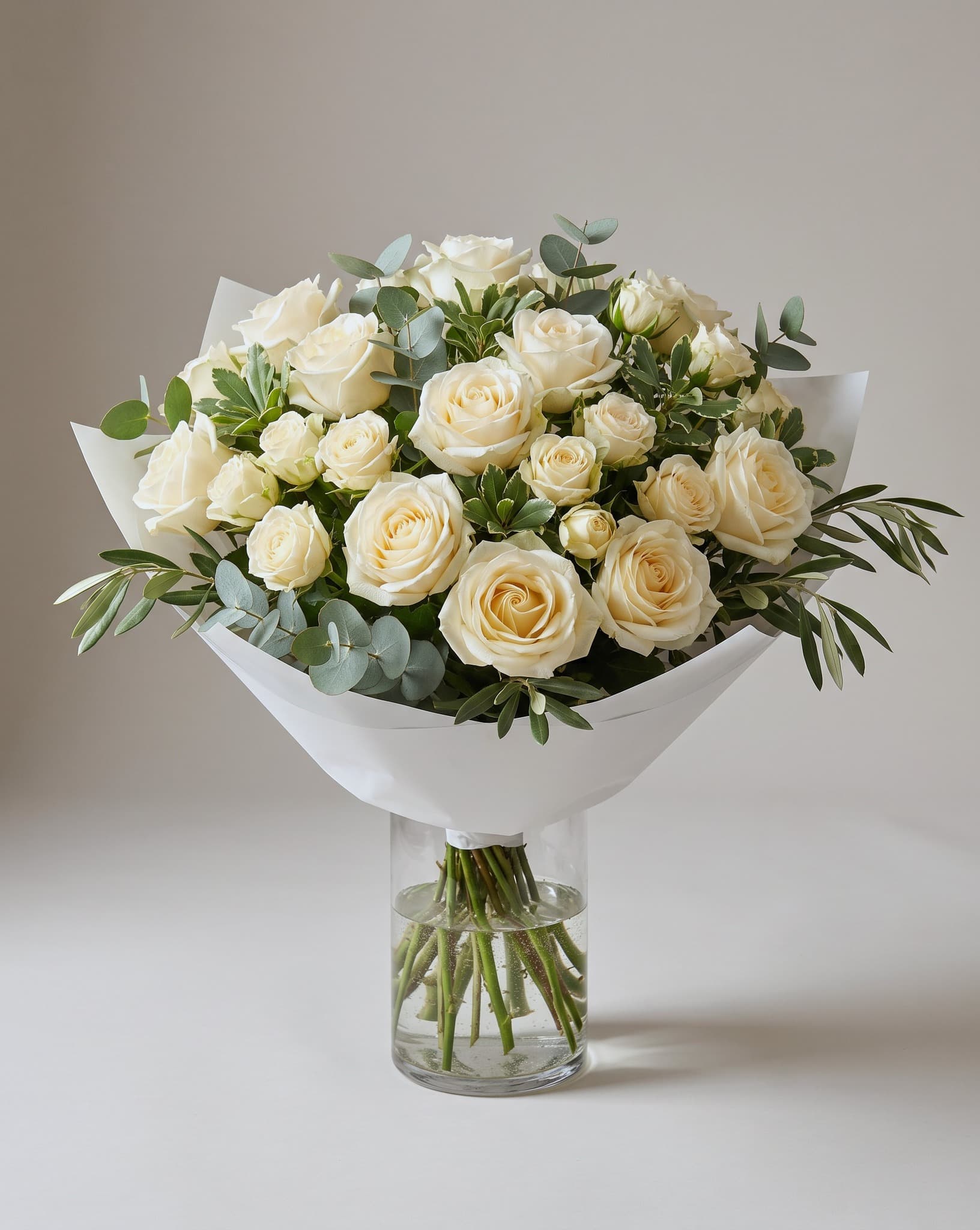 Rosas crema con eucalipto envueltas en papel blanco, en un florero de vidrio transparente