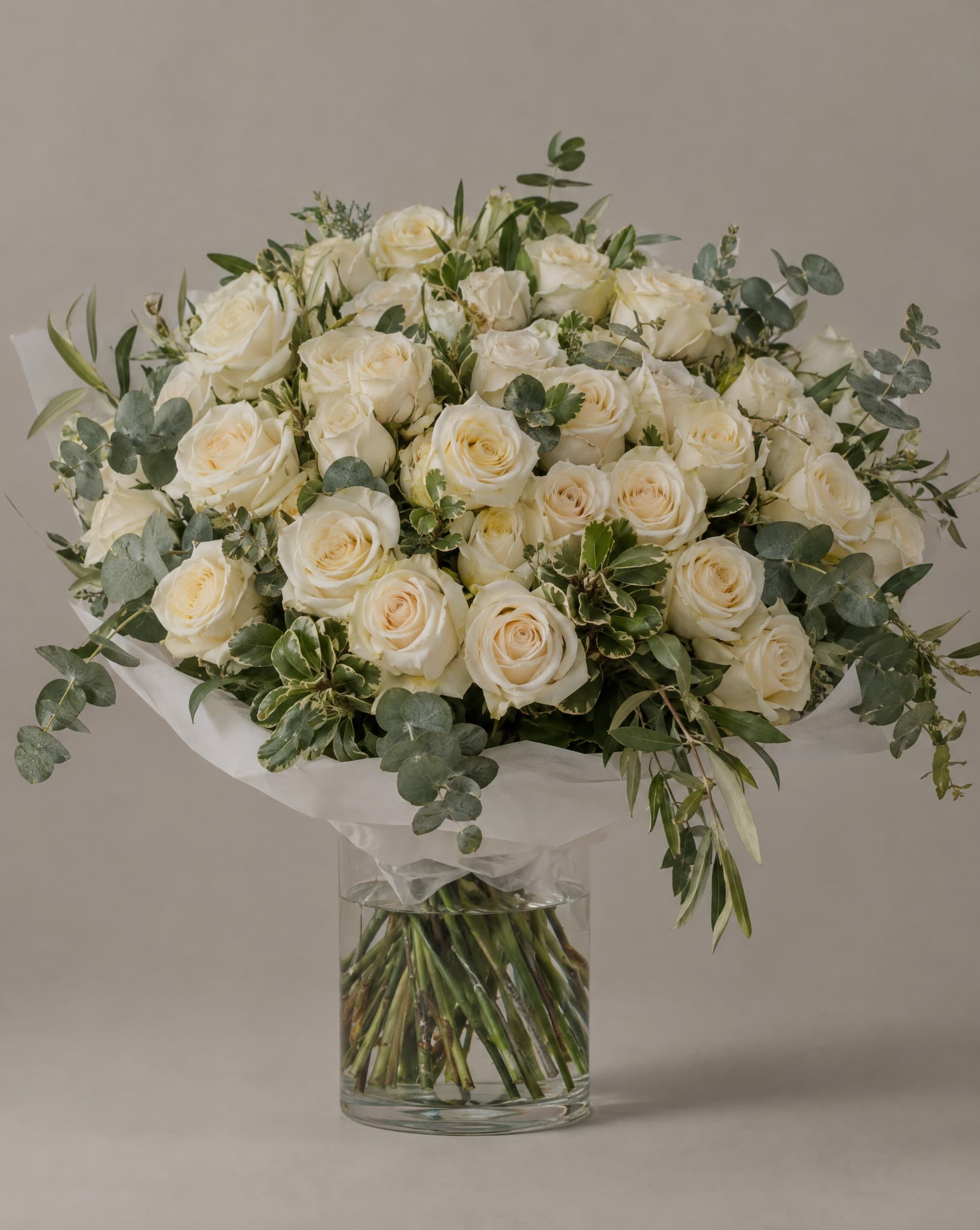 Rosas crema con eucalipto envueltas en papel de seda blanco, en un florero de vidrio transparente