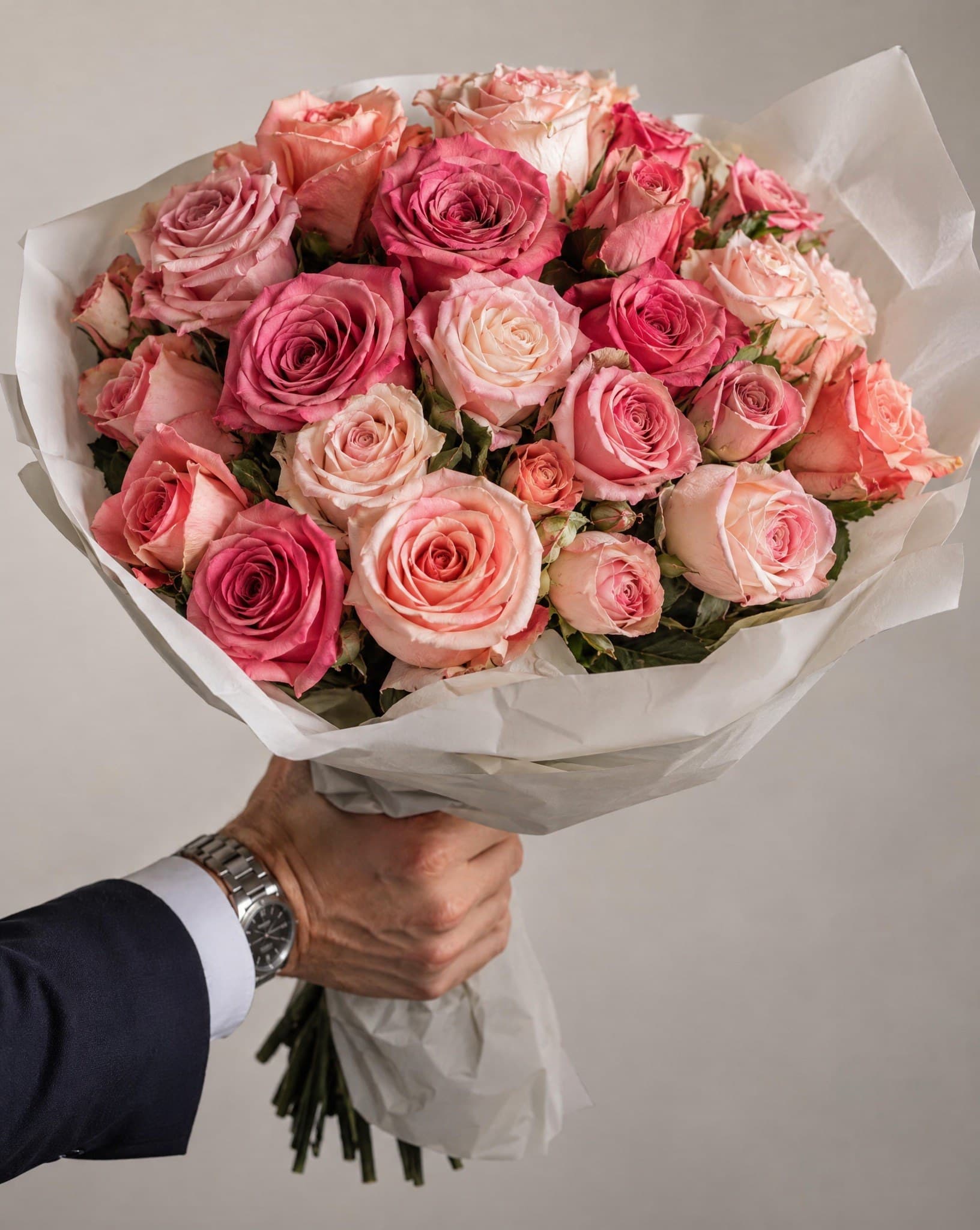 A man in a suit holding out a large bouquet of pink roses
