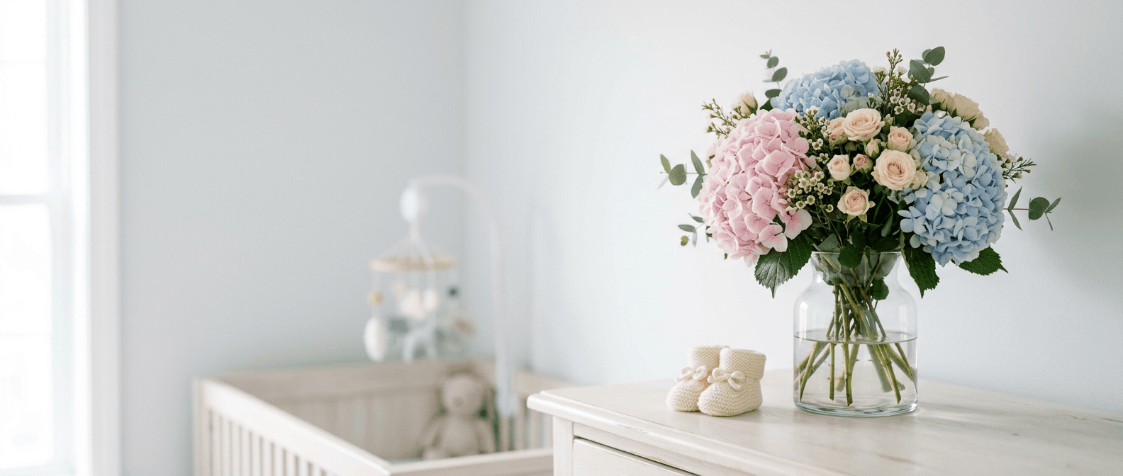Pastel hydrangeas and spray roses beside a knitted baby bootie