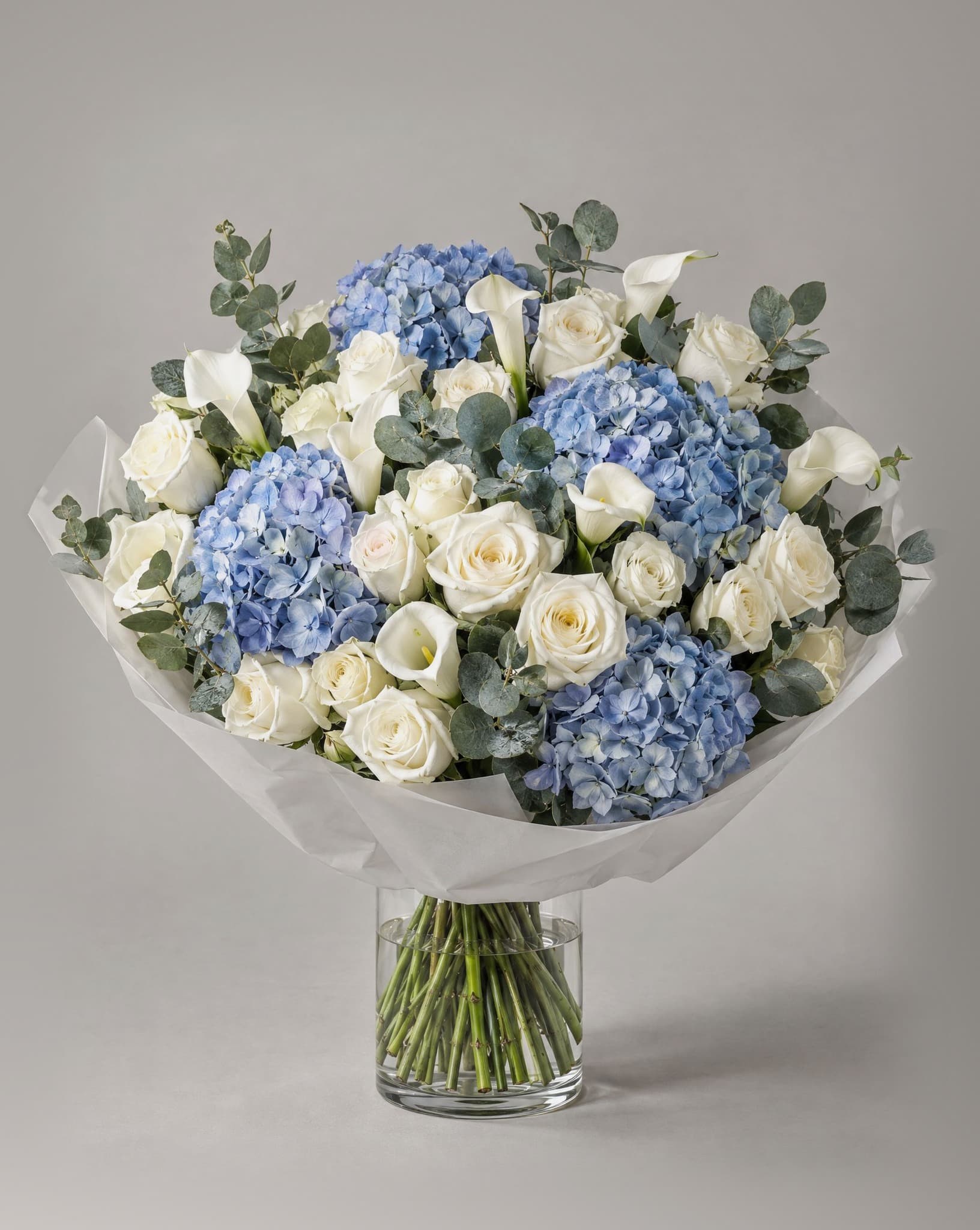 Grand bouquet of blue hydrangeas, white roses and white calla lilies with eucalyptus in a clear glass vase