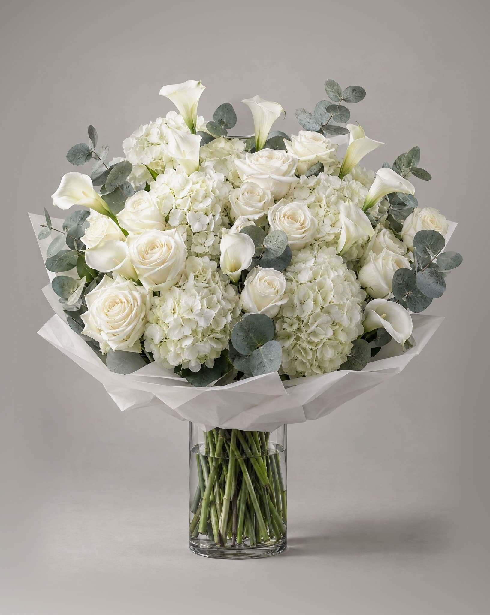 Grand bouquet of white hydrangeas, white roses and white calla lilies with eucalyptus in a clear glass vase