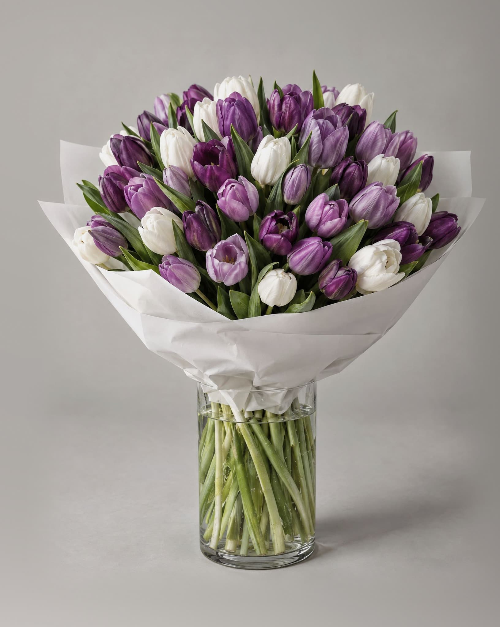 Grand bouquet of purple, lilac and white tulips wrapped in white paper in a clear glass vase